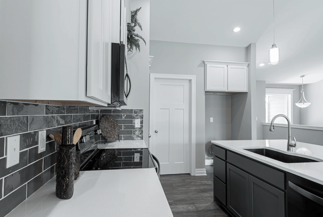 Modern kitchen with white cabinets, black tile backsplash, quartz countertops, and stainless steel fixtures